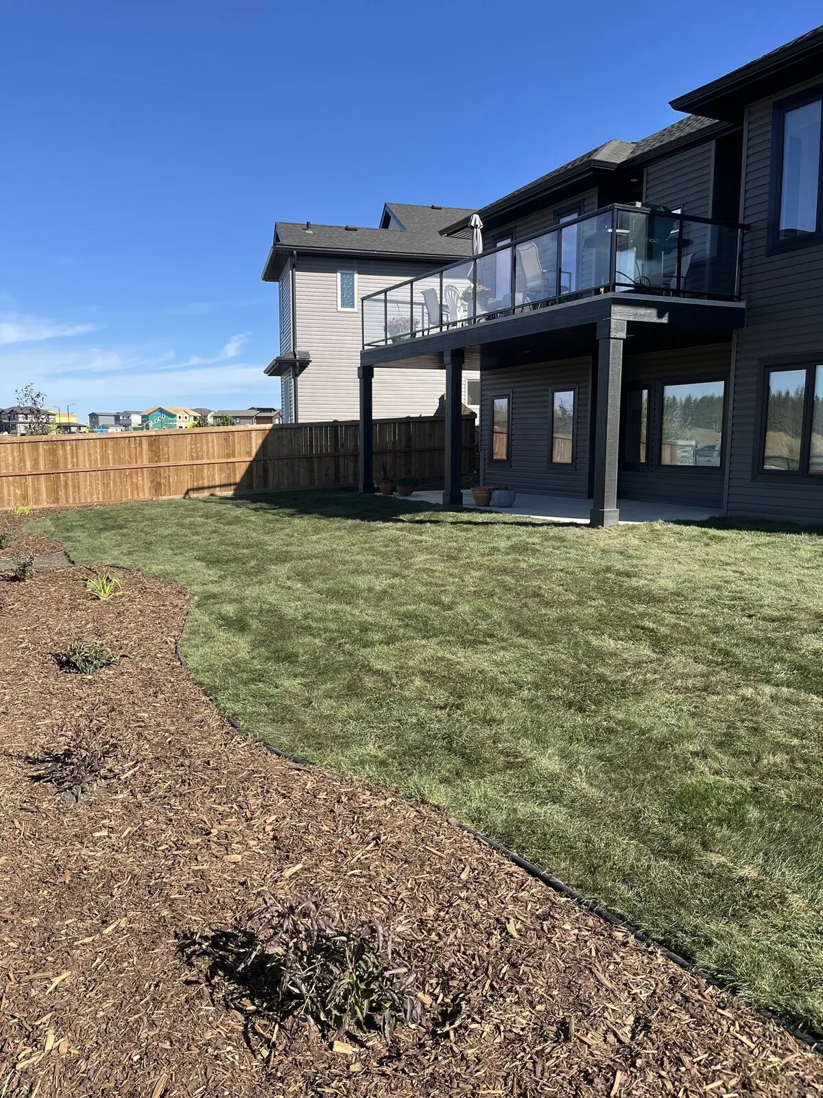New-build backyard with a curved mulch bed, fresh sod and a cedar fence