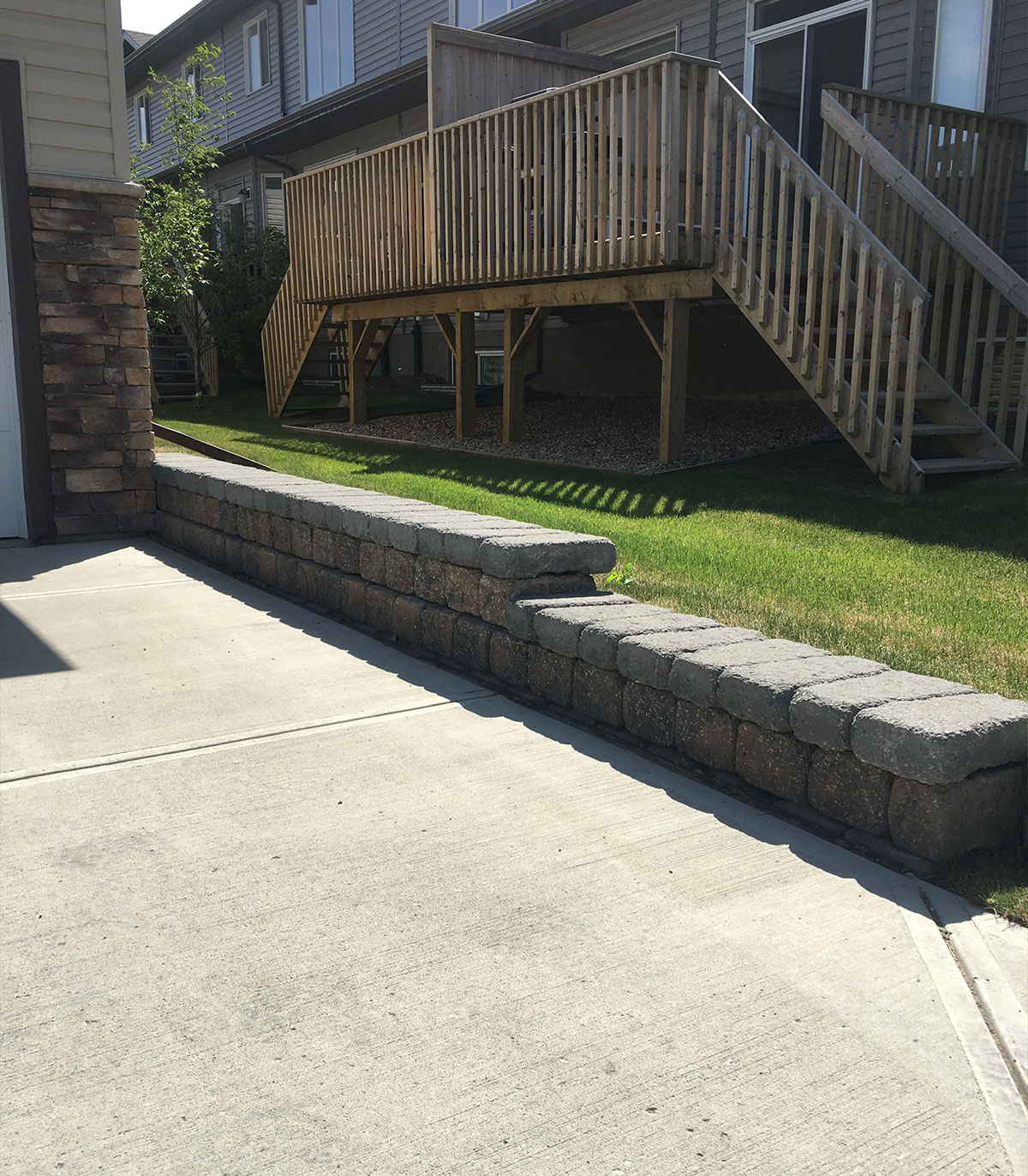 Block retaining wall beside a concrete walkway below a raised deck